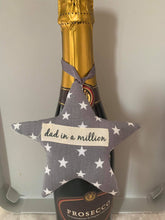 Load image into Gallery viewer, A softly padded star or heart with looped ribbon - so perfect for hanging around the bottle of something when gifting.  They can then choose where to hang it afterwards.  Choose your message - &#39;Dad in a Million&#39;, &#39;Grandad in a Million&#39; or &#39;Happy Father&#39;s Day&#39;  Fabric options are - grey stars, football, Union Jack or rugby - I have many more options so please use the &#39;Contact Us&#39; page if you would like to discuss these.
